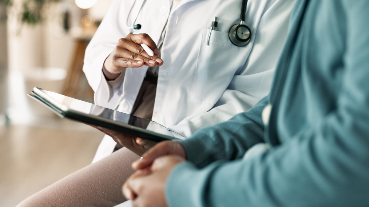 A clinician holding a digital device discuss a diagnosis with someone.