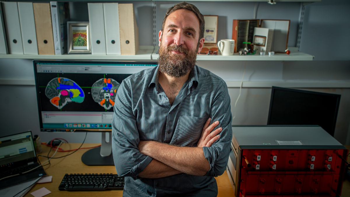 Professor Lorenzo Fabrizi, one of our Changing Policy and Practice awardees. He stands in front of a computer with a brain scan image.